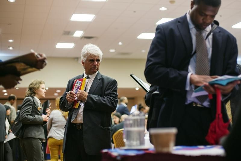 A man walks past job seekers as they fill out job applications for recruiters during a job fair in New York